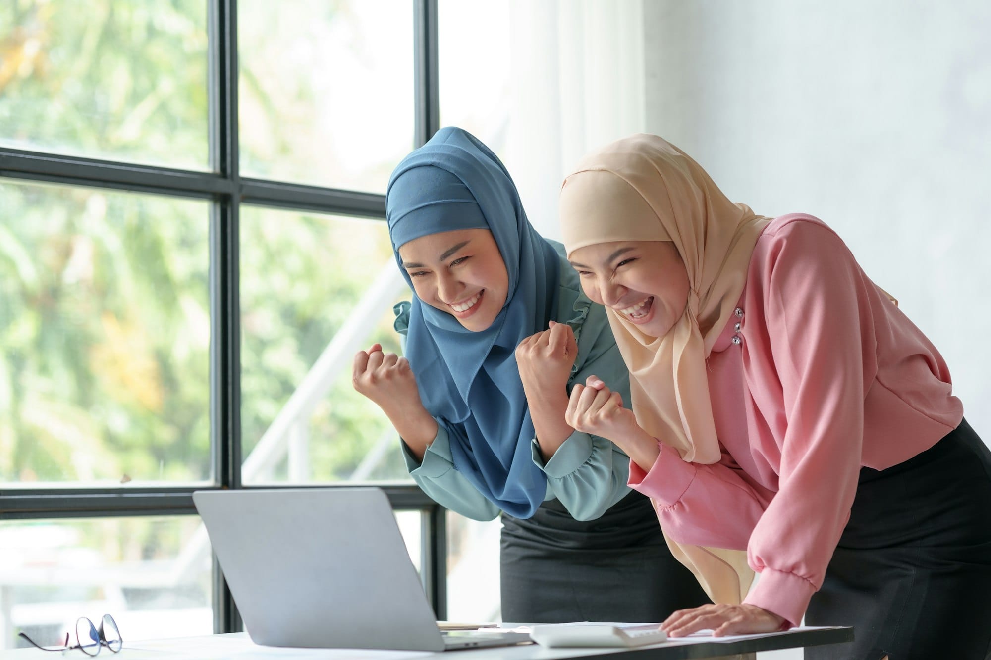 Two beautiful Muslim Asian businesswomen wearing hijab rejoice at their work accomplished with happy
